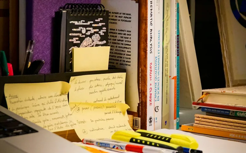 Study desk with sticky notes, highlighters, a laptop and a row of books