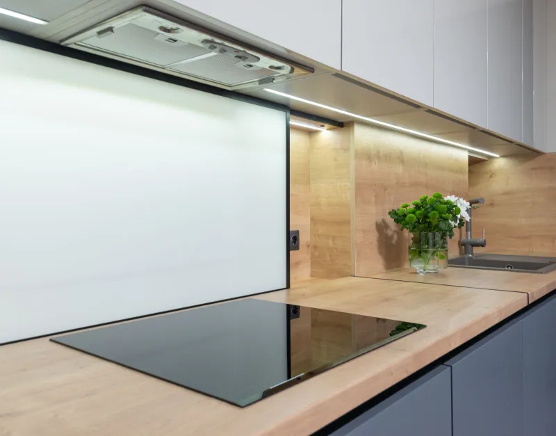 A black glass hob set into a wooden worktop beneath a cooker hood in a modern kitchen
