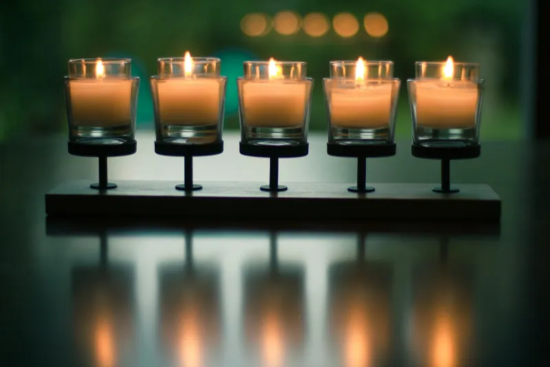 Candles Direct: half-price Yankee Candle gift sets and cheaper large jars Five lit candles in glass holders on a wooden stand, reflected in a dark table