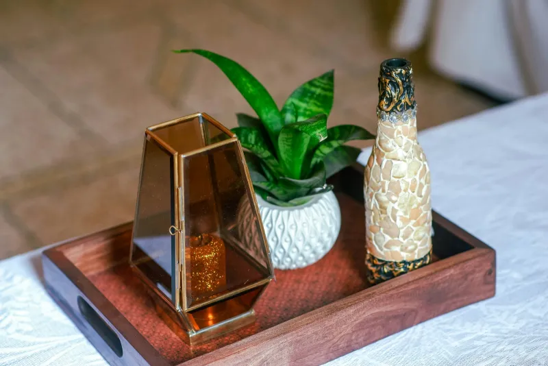 Candle lantern, potted plant and decorative bottle arranged on a wooden tray