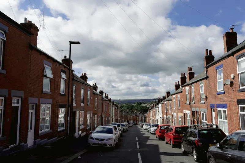 Cars parked along a street of red brick terraced houses