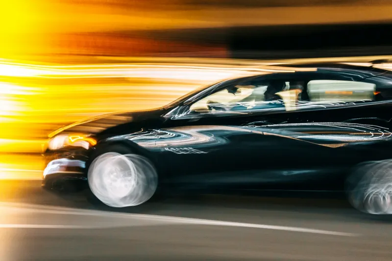 Black car driving at night with streaks of yellow light behind it