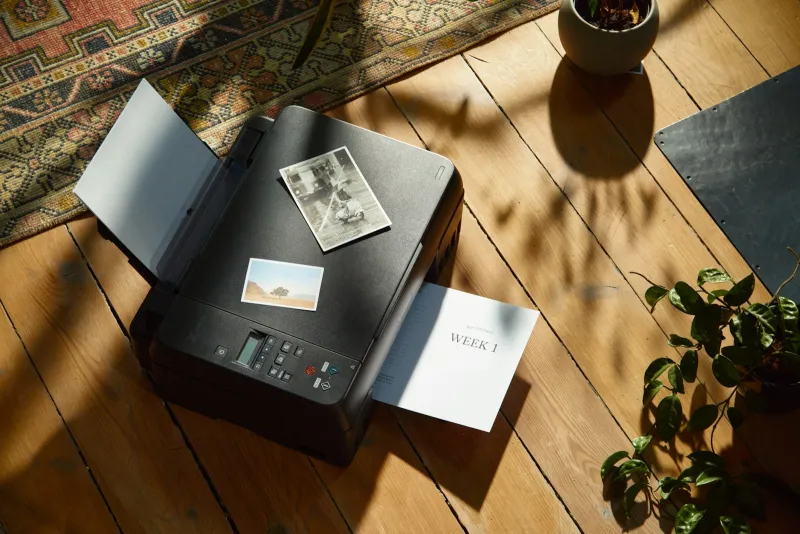 Home printer on a wooden floor with printed photos and a plant