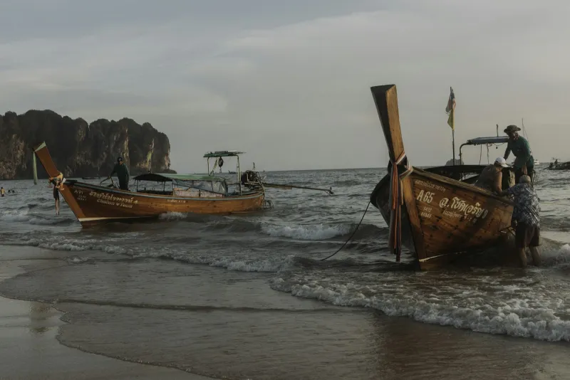 Two Thai longtail boats resting on a sandy beach in Krabi