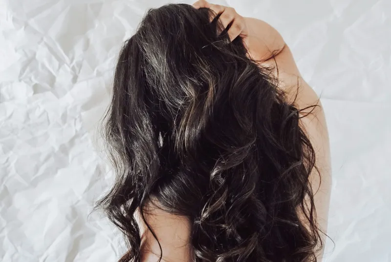 The back of a woman's head with long, wavy dark brown hair against a white background