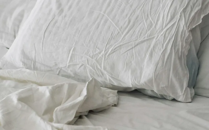 A rumpled white duvet and pillow on a bed in soft morning light