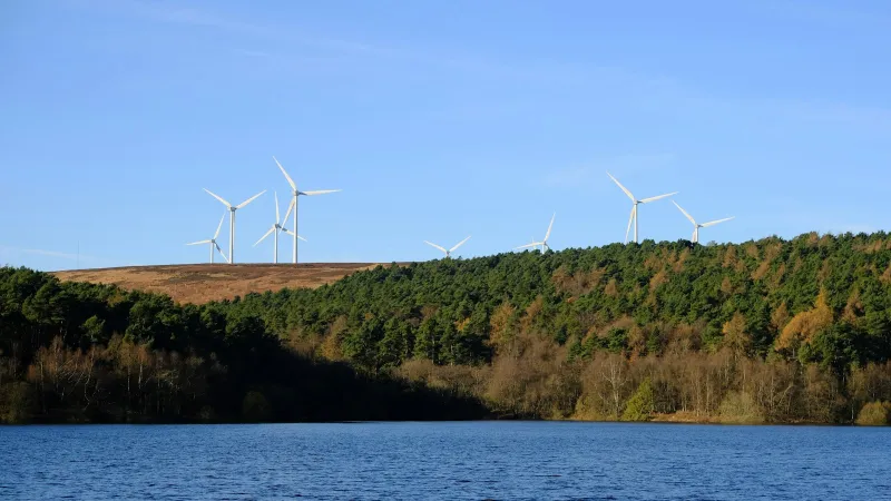 Wind turbines on a moorland ridge above woodland and a reservoir