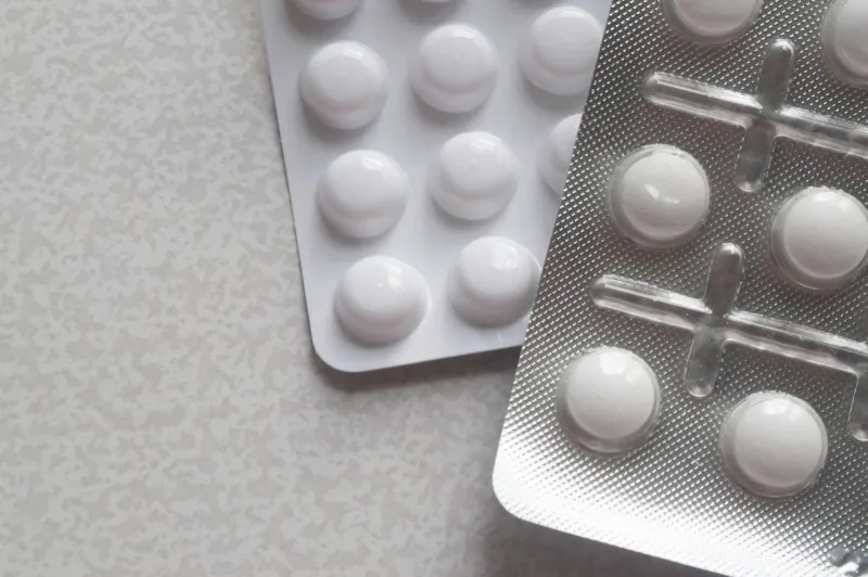 Two blister packs of white tablets on a pale speckled table