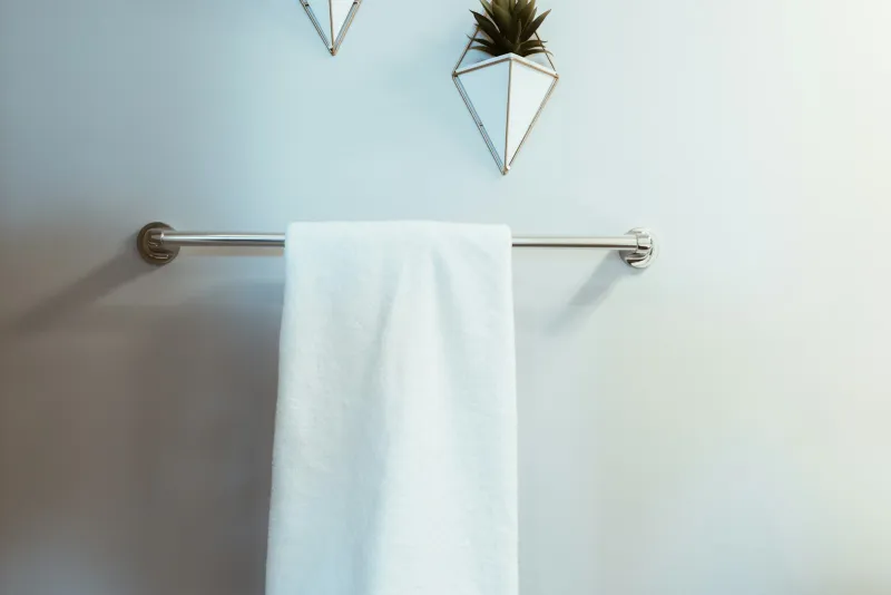 A white towel hanging on a chrome towel rail on a pale bathroom wall
