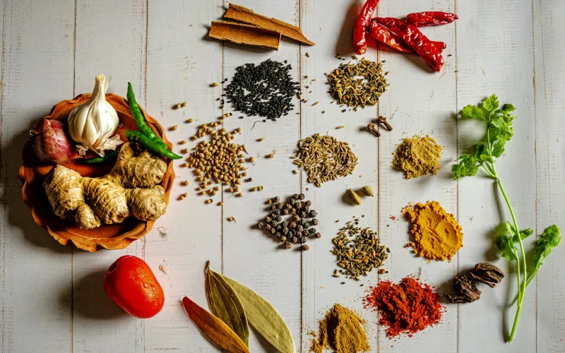 Little heaps of whole and ground spices, chillies, ginger and garlic on a pale wooden table