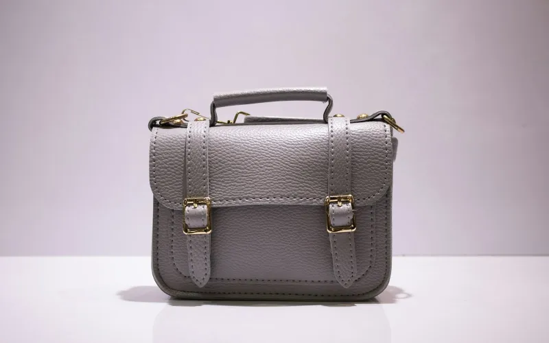 A grey leather satchel with gold buckles on a white surface