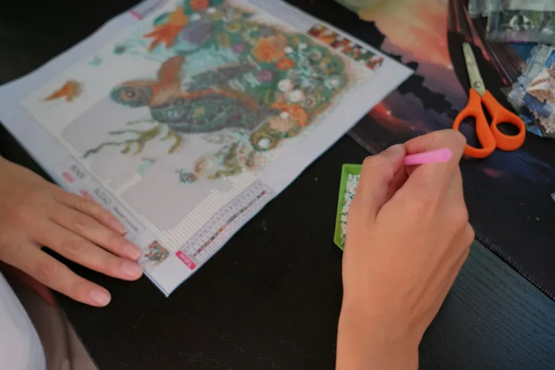 Hands placing gems on a sea turtle diamond painting at a table