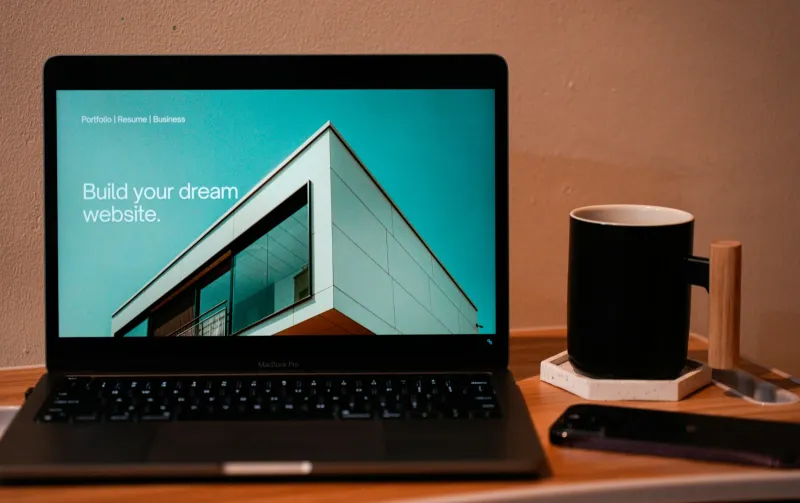 Laptop on a wooden desk showing a website template next to a black mug