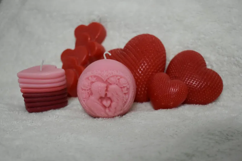Pink and red heart-shaped candles on a soft white blanket