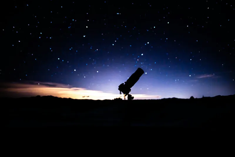 Silhouette of a telescope against a starry night sky at dusk
