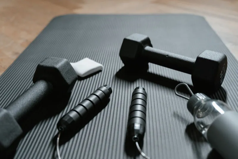 Dumbbells, a skipping rope and a water bottle on an exercise mat at home