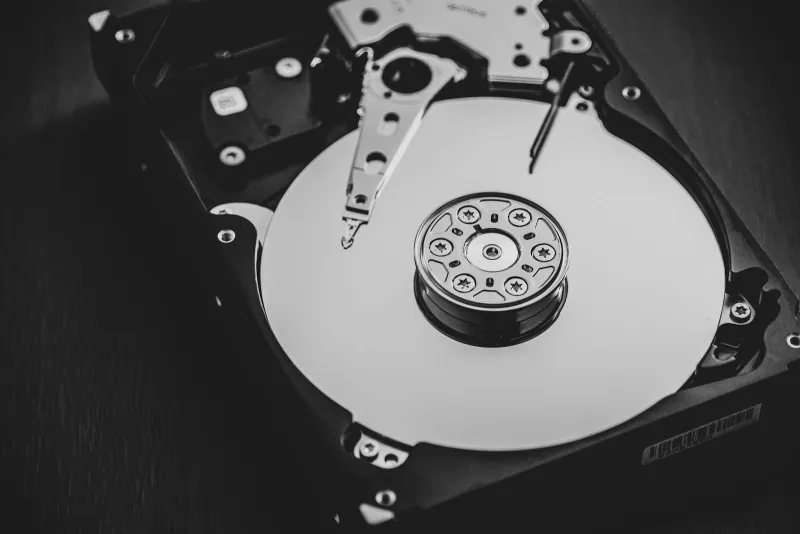 An opened hard disk drive showing its platter and read arm, in black and white