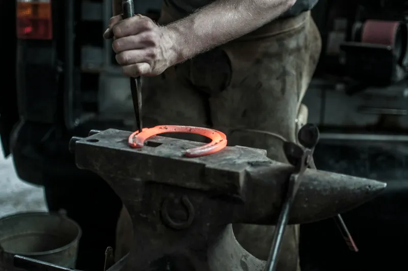 A horseshoe glowing orange on an anvil as a smith works it with a tool