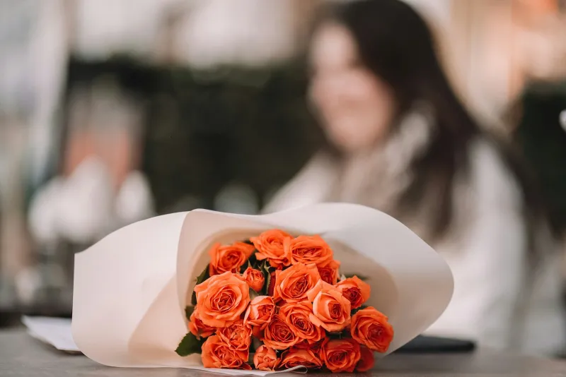 A bouquet of orange roses wrapped in white paper on a table