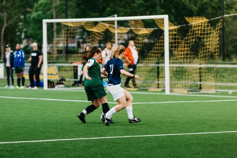 EmPowerBall: grassroots football kit and league merch, made to order Two women's football players chasing the ball near a goal on an artificial pitch
