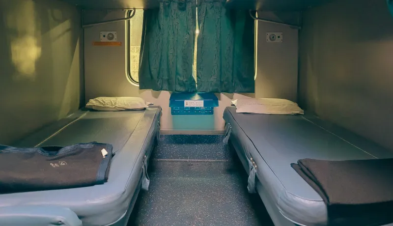 Two made-up berths in a train sleeper compartment with green curtains at the window