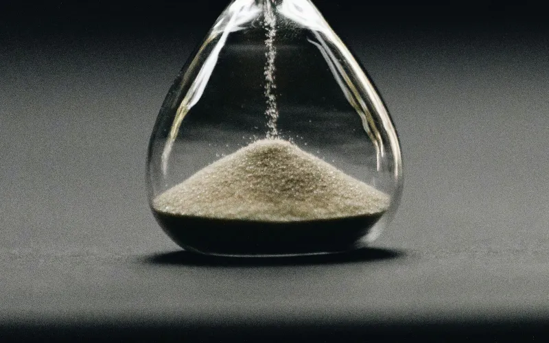 Sand running through a glass hourglass against a dark grey background