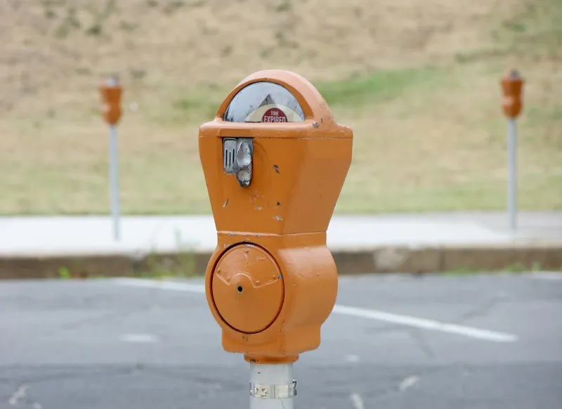 An orange coin parking meter beside an empty car park, with more meters in the background