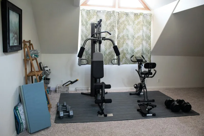 A home gym in a loft room with a multi-gym, exercise bike and dumbbells on floor mats