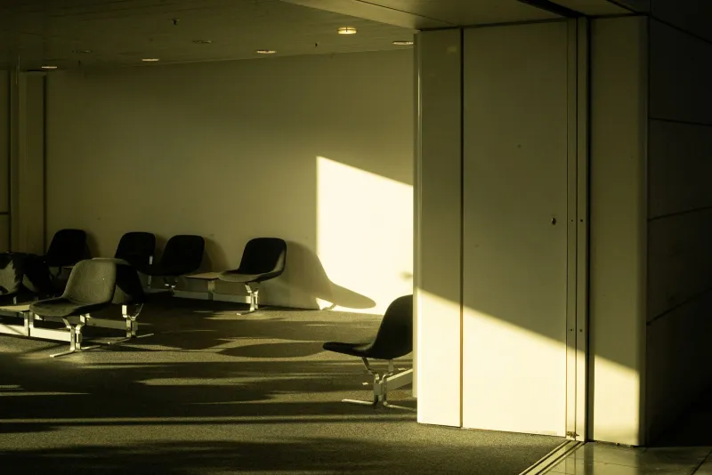 Empty seats in an airport waiting area, lit by low sunlight falling across the wall and floor