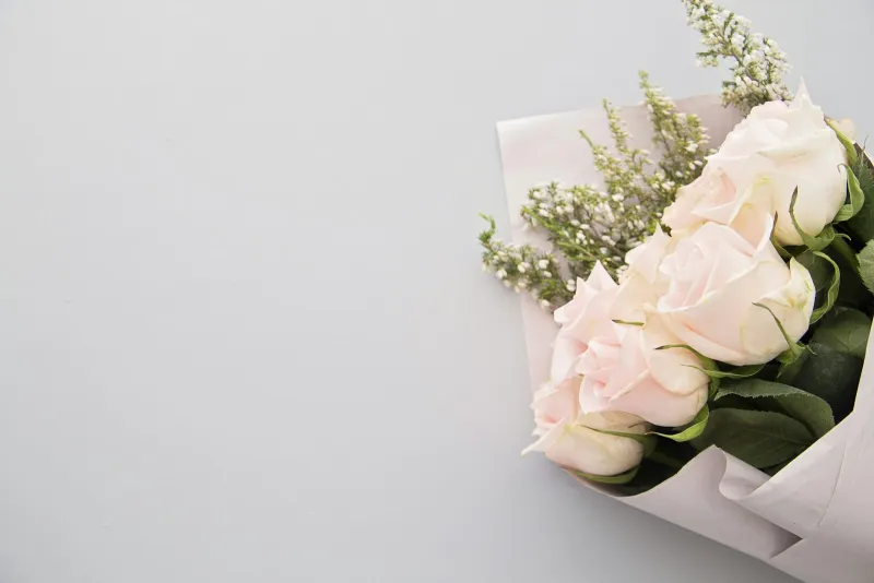 A bouquet of pale pink roses and white filler flowers wrapped in paper on a grey surface