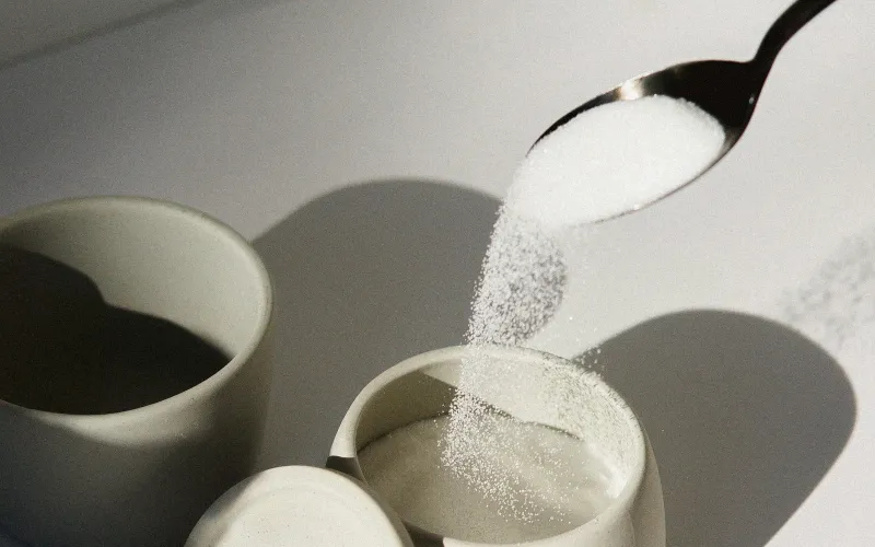 Sugar pouring from a spoon into a white ceramic cup