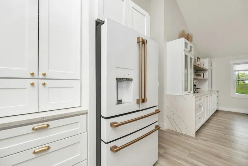 French Furniture Fittings: handles and knobs from a Wiltshire family firm White shaker kitchen cupboards with brass cup handles and round knobs beside a fridge with copper handles