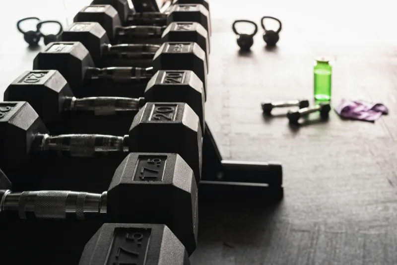 Rows of black hex dumbbells on a rack with kettlebells on a gym floor