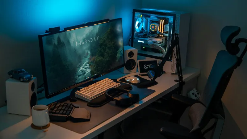 A desktop gaming setup with monitor, keyboard, headphones and a lit PC tower
