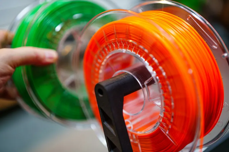 Orange and green spools of 3D printer filament on a holder