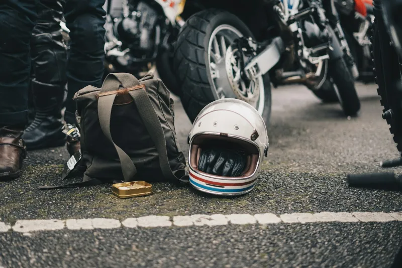 GhostBikes: motorcycle helmets, gloves and kit with free delivery over £25 A white open-face motorcycle helmet and a canvas backpack on the tarmac beside parked motorbikes