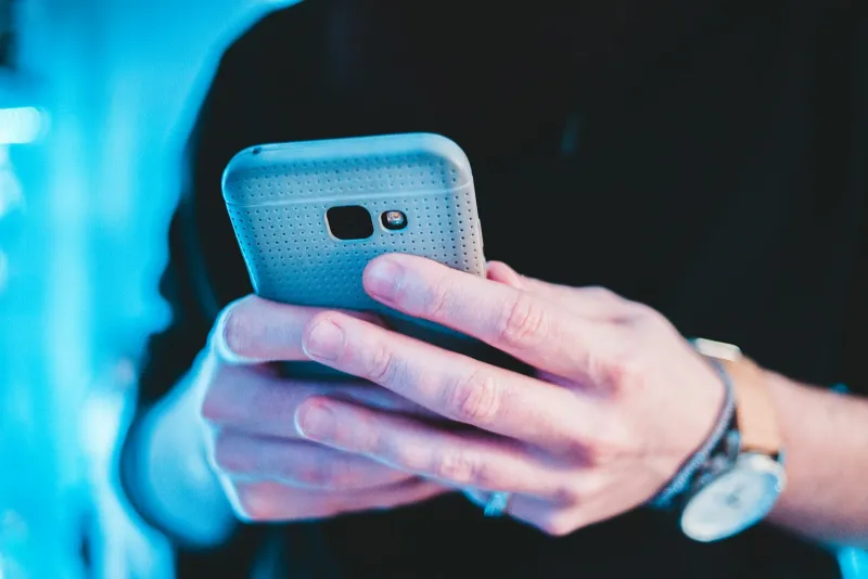 Close-up of hands holding a smartphone against a blue-lit background