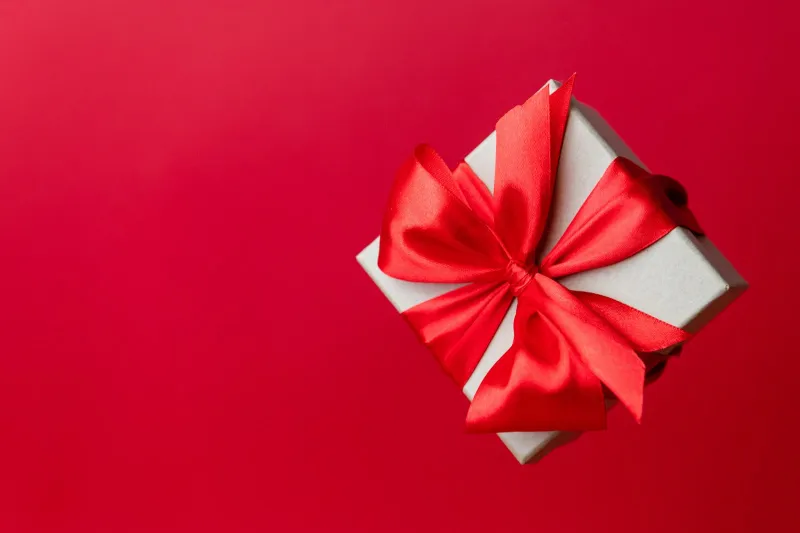 A small white gift box tied with a red satin bow on a plain red background