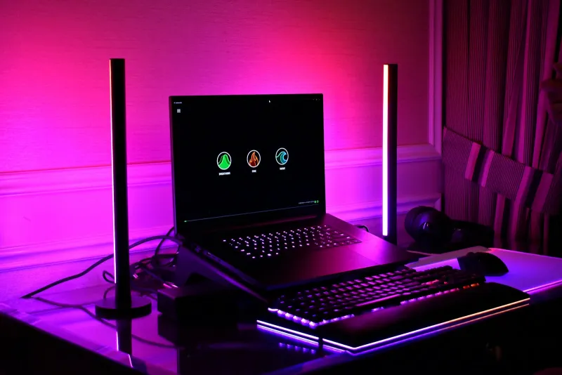 A desk with a laptop and keyboard lit pink and purple by two upright LED light bars