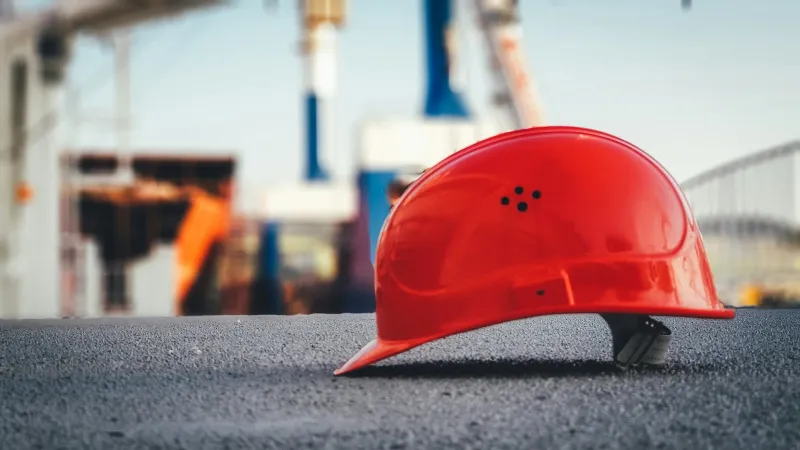 A red safety helmet on tarmac with a blurred construction site behind