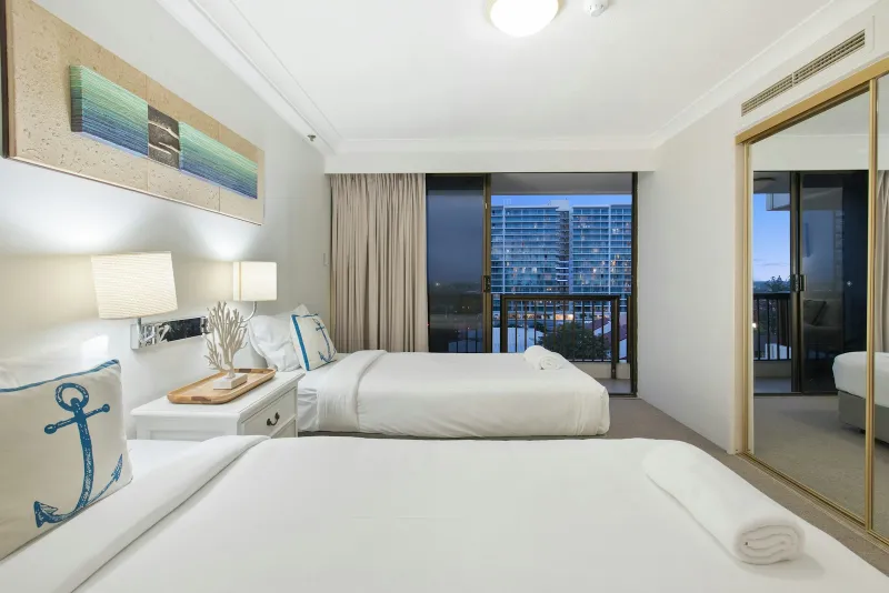 Two made-up beds with white linen in a bright apartment bedroom