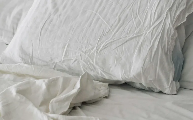 White pillow and rumpled white bedding on a bed