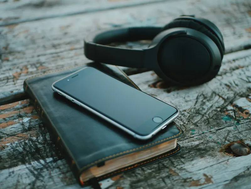A smartphone resting on a leather-bound book beside a pair of black headphones