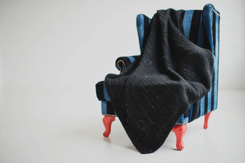 A black knitted blanket draped over a blue striped wingback armchair against a white wall