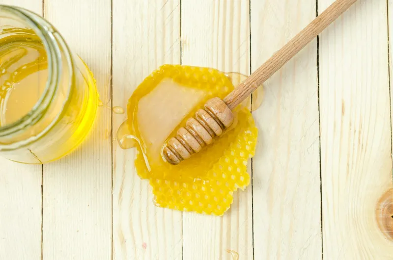 Wooden honey dipper resting on a piece of golden honeycomb