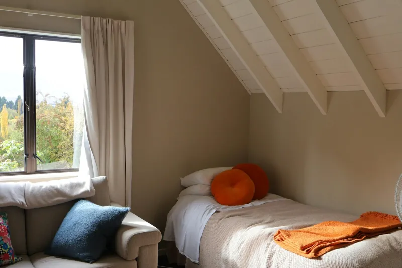 A small attic spare room with a single bed, a sofa and a window looking out on autumn trees