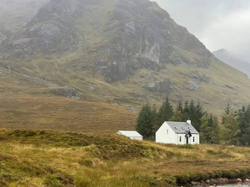 A small white cottage below a misty mountain in a Scottish glen
