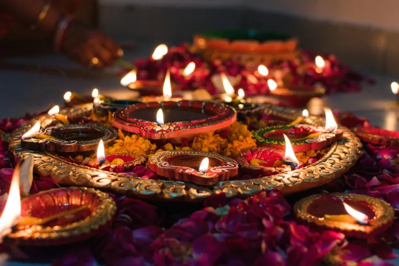 Lit clay diyas on a decorated tray surrounded by rose petals and marigolds