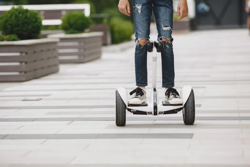 Rider in jeans and trainers standing on a white self-balancing board on a paved path