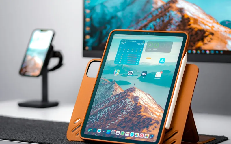A tablet in an orange case and a phone on a stand on a desk
